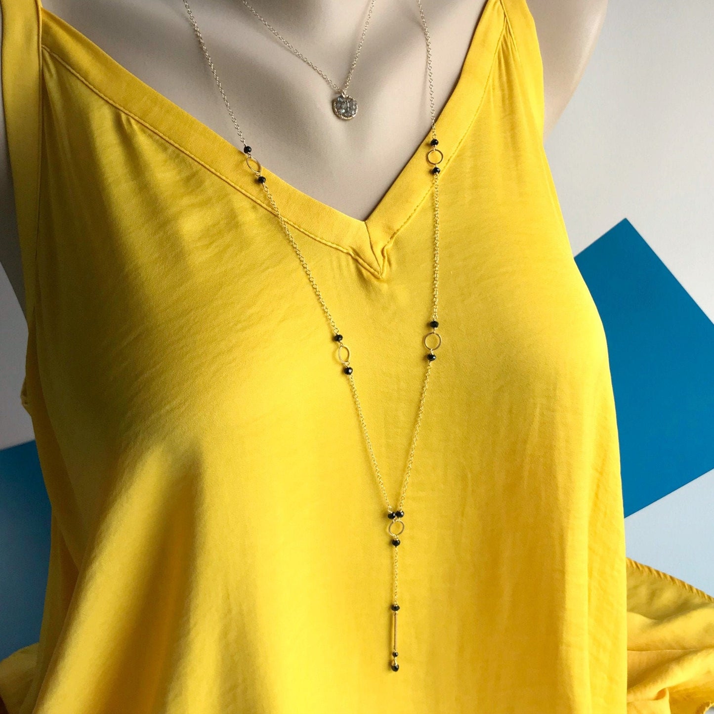 Crafted from 14K gold-filled and sterling silver, this necklace measures 31 1/2 inches in total length and offers versatility for various occasions. The unique design extends to the clasp, where two tiny beads add a touch of color, ensuring that the necklace looks great from behind—ideal for styling your hair up.