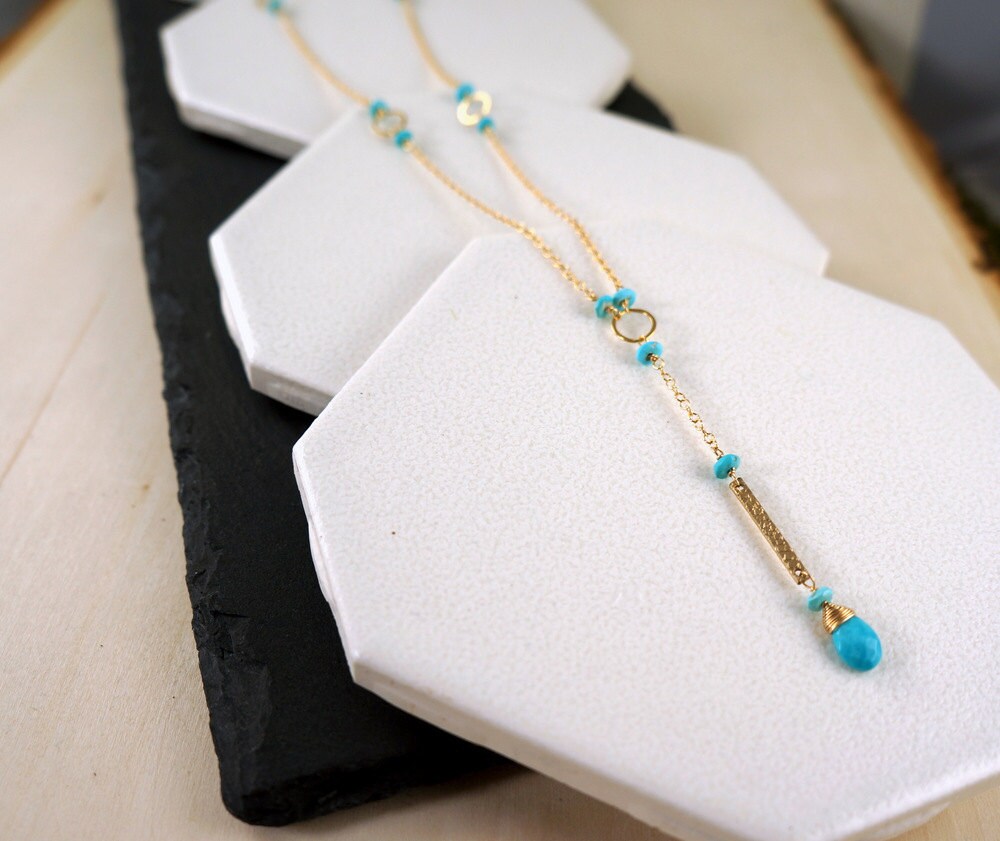 Close-up view of a turquoise Y-bar necklace with a silver or gold chain, showcasing the pendant design and color